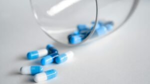 A close-up of blue and white capsules spilling from a glass on a light background.